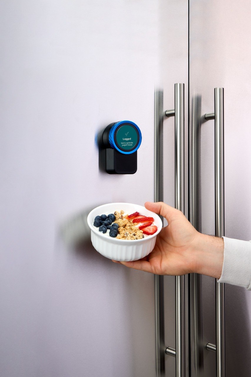 Trepo mounted on a fridge door, its display confirming a berry granola yogurt bowl has been logged
