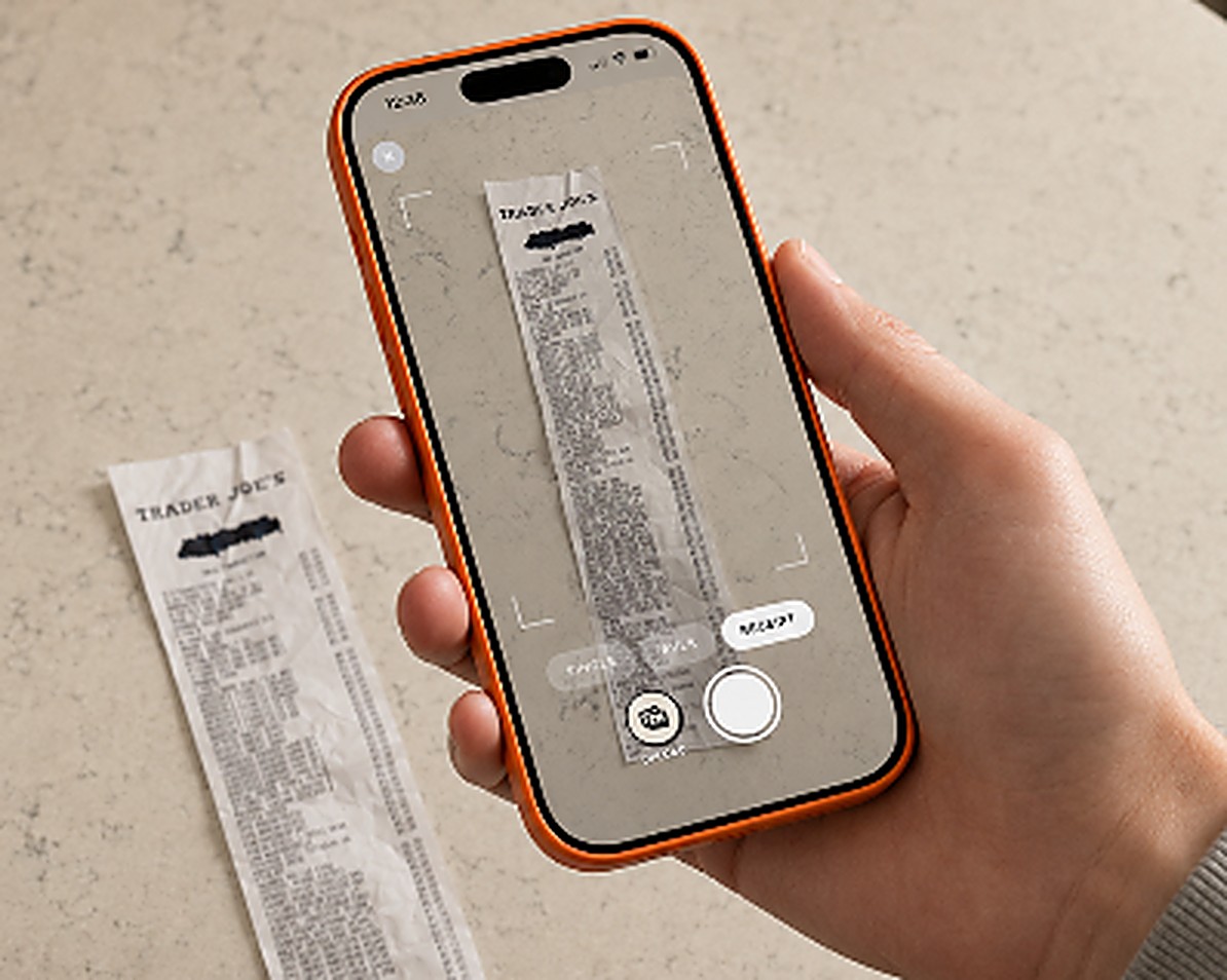 A hand holding a phone over a kitchen worktop, photographing a Trader Joe's receipt inside the Trepo capture frame