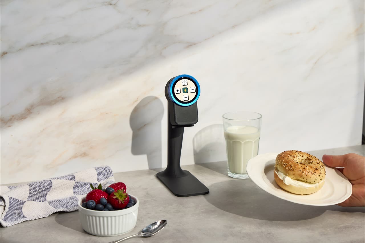 The Trepo device on its countertop stand, a plate with a bagel and cream cheese being held up to it to read the macros